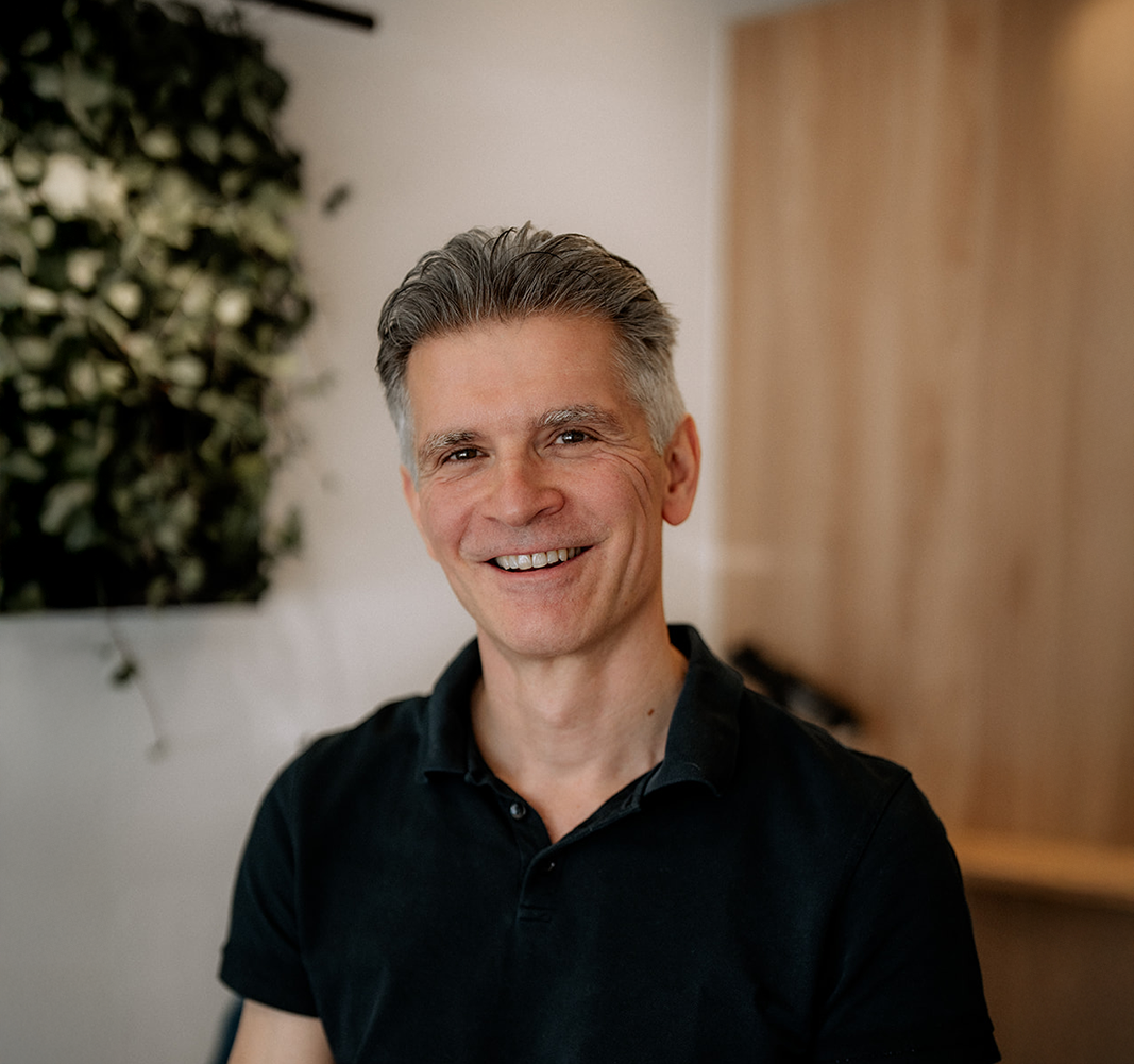 Porträt eines lächelnden, plastischen Chirurgen, der in Schönheitsklinik an seinem Schreibtisch sitzt. (Wettstein Ästhetik und Chirurgie)