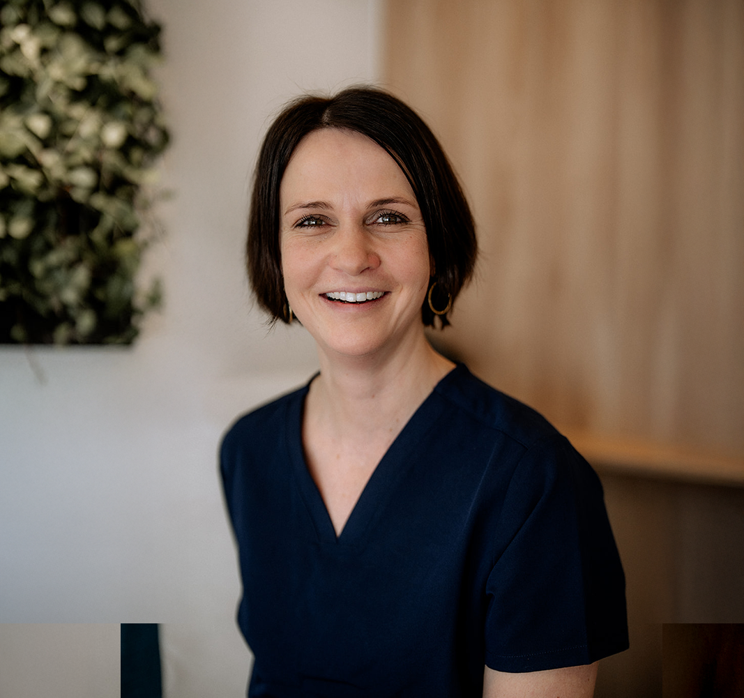 Porträt einer lächelnden, dunkelhaarigen Mitarbeiterin einer Schönheitsklinik vor einer weissen Wand. (Wettstein Ästhetik und Chirurgie)