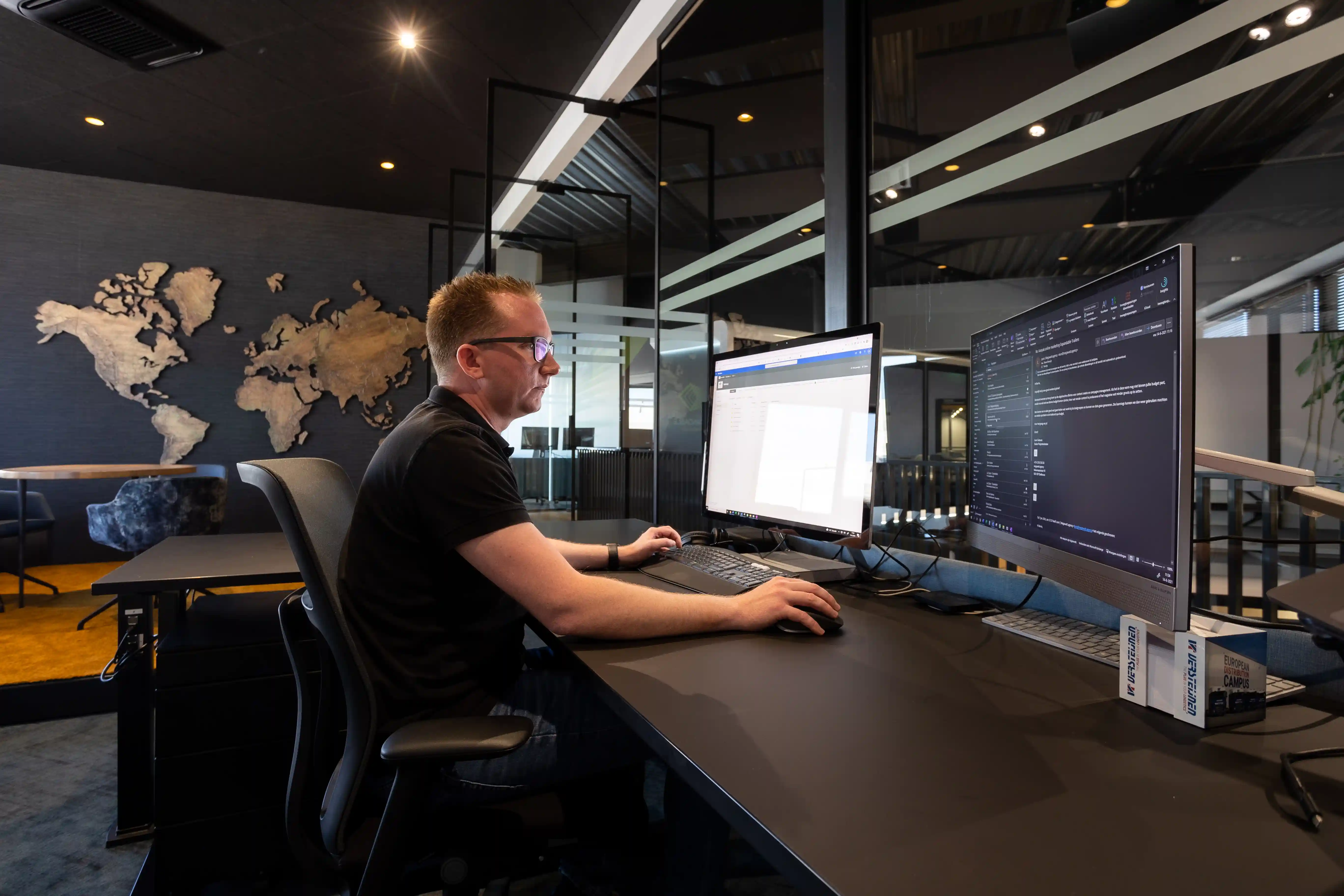 A Supply Chain & Article Management Specialist working at a desk with dual monitors in a modern office, analyzing product data and managing inventory systems, with a world map in the background.