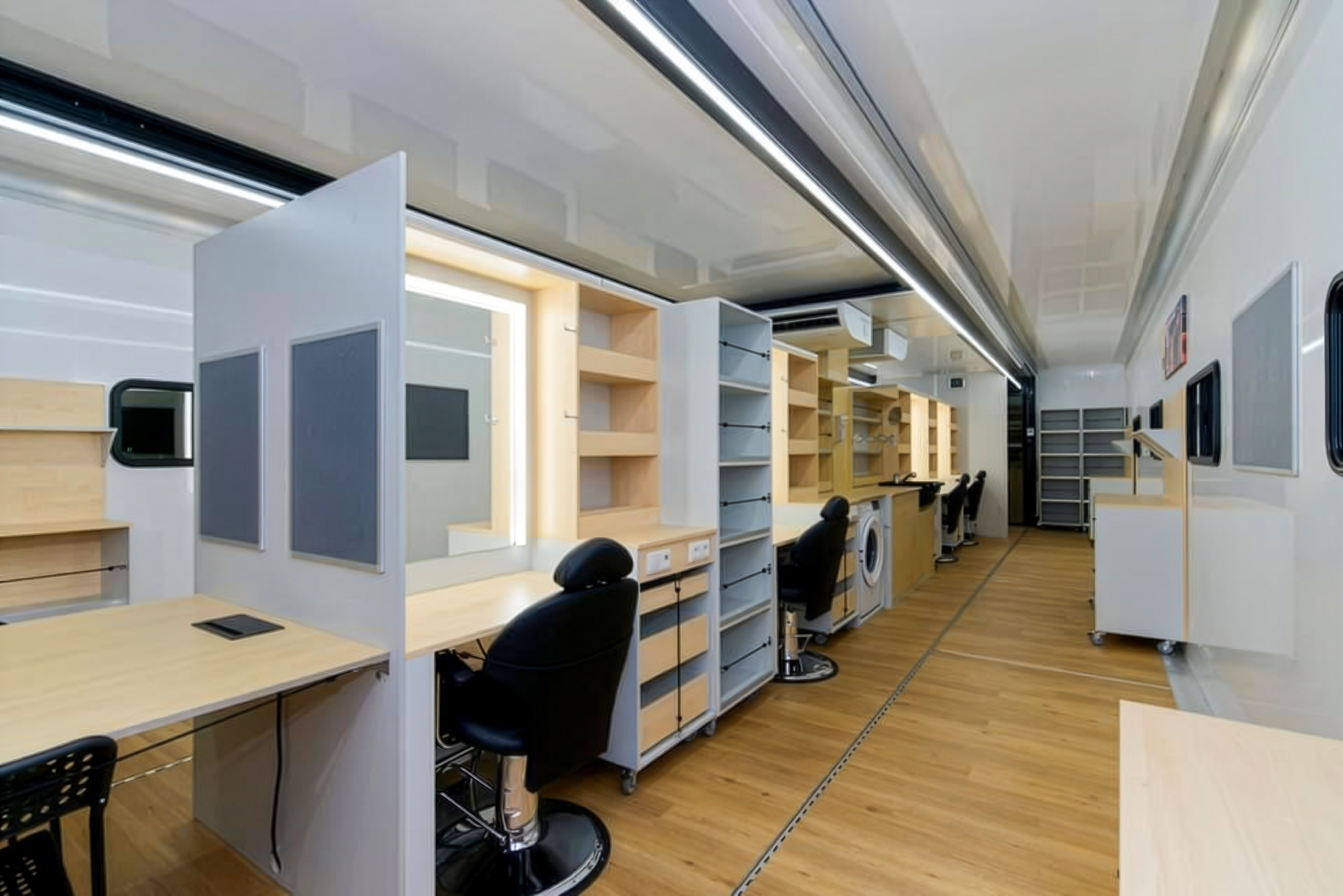 À l'intérieur de la roulotte de coiffure et de maquillage, un couloir bien éclairé avec des miroirs et des armoires blanches modernes, une buanderie et un élégant espace de travail noir sur plan de travail.