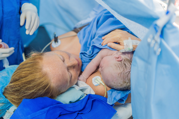 A woman holding her newborn baby after a C-section. There are medical personnel around her.