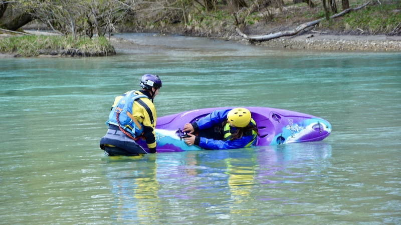 instructor helps woman in a whitewater kayak to reroll her kayak on the sava river
