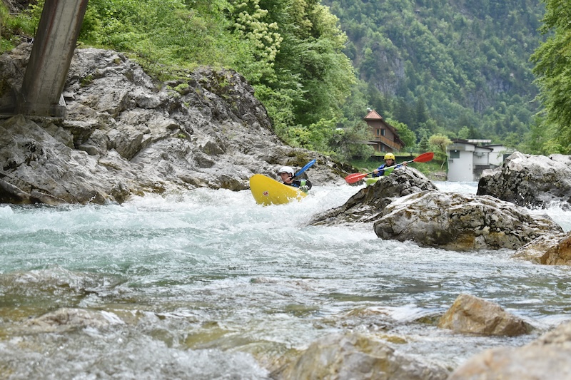 two kayakers going through a rapid in bled slovenia surrounded by trees and bush