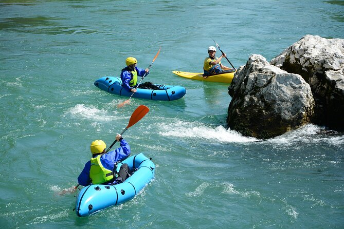 Three people wearing helmets and life jackets paddling downriver in inflatable packrafts on a river near rocks.