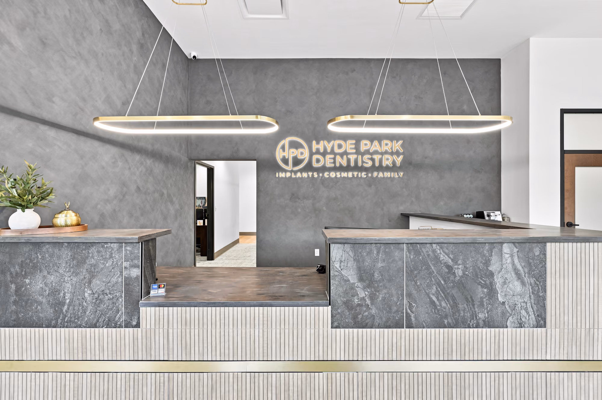 Modern dental reception area with stone counter, two large pendant lights, and Hyde Park Dentistry sign.