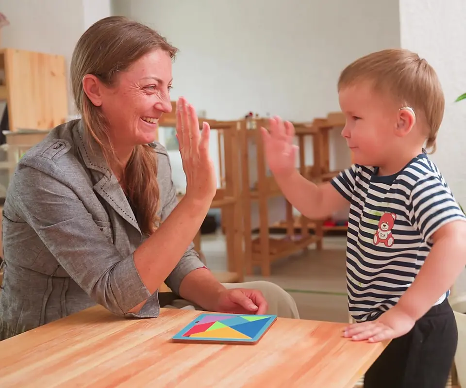 Nursery practitioner sharing a high five with a young child over a puzzle