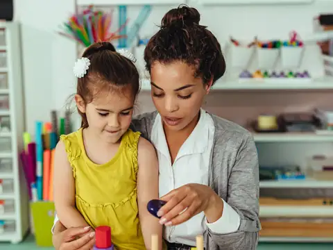 Teacher helping a girl build a tower of stacking shapes