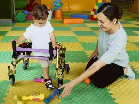 Young child using a walking frame while a practitioner plays with them
