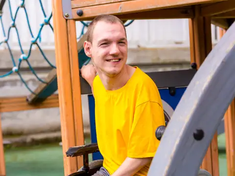 Smiling young man in a wheelchair at an outdoor play area