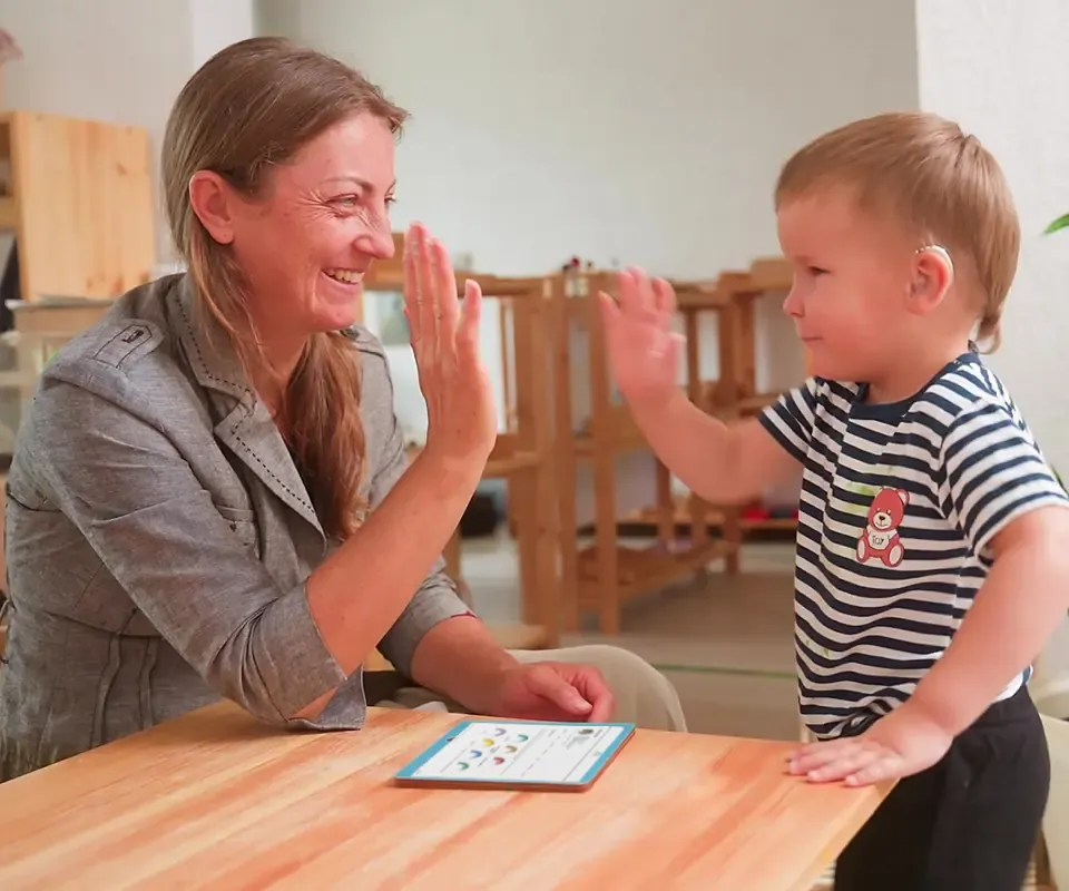 A teacher sharing a high five with a young child, with Arc Pathway open on a tablet