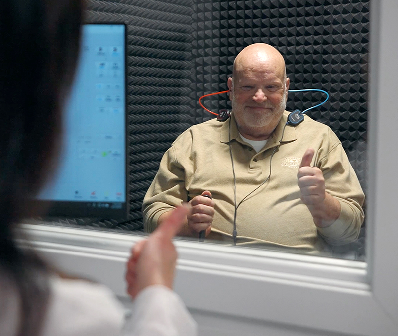 Image of a patient showing a thumbs up during a comprehensive hearing exam in a booth