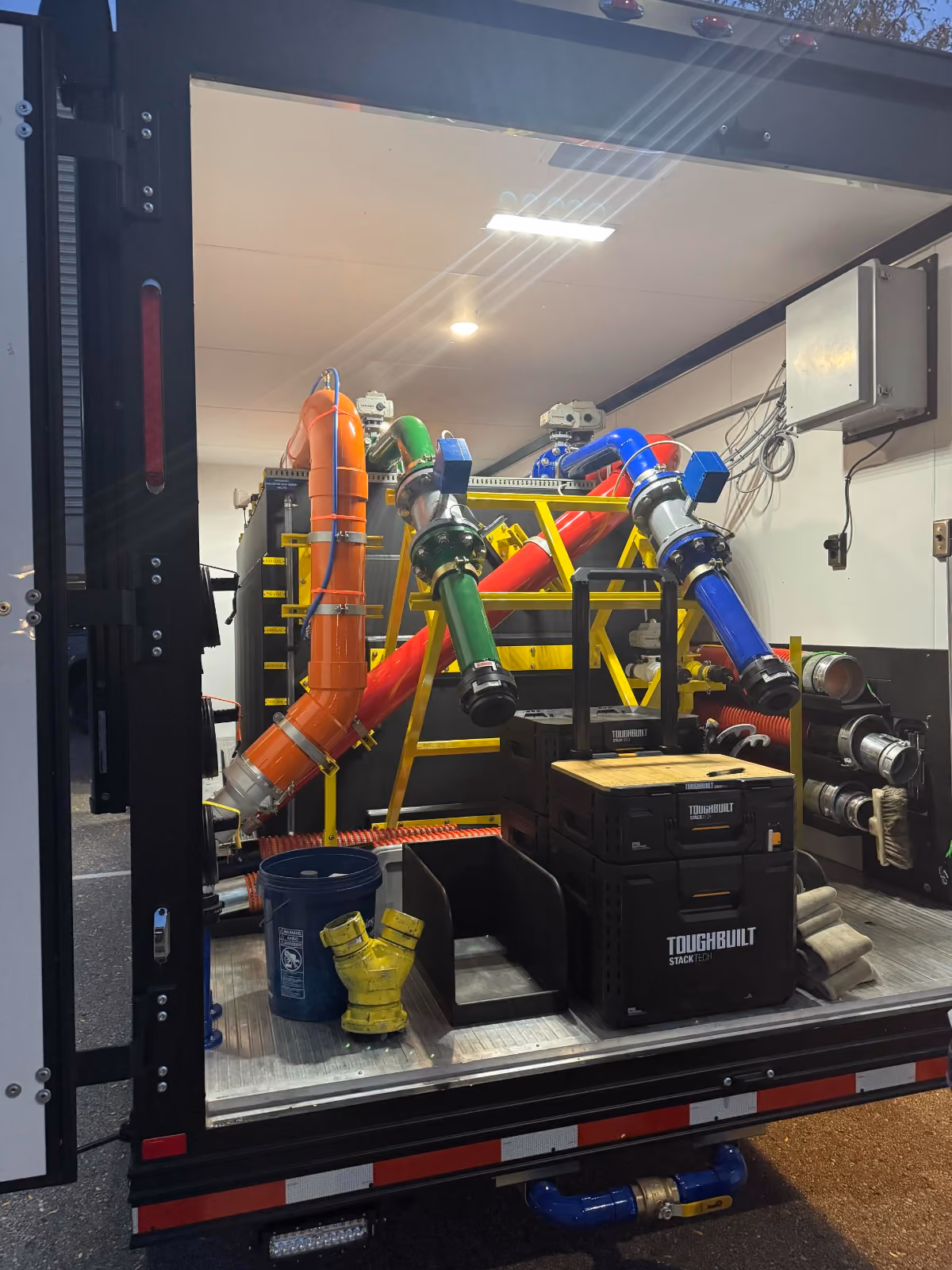 The interior of a trailer is filled with colorful decontamination equipment, hoses, ToughBuilt toolboxes, and various fittings organized for easy access.