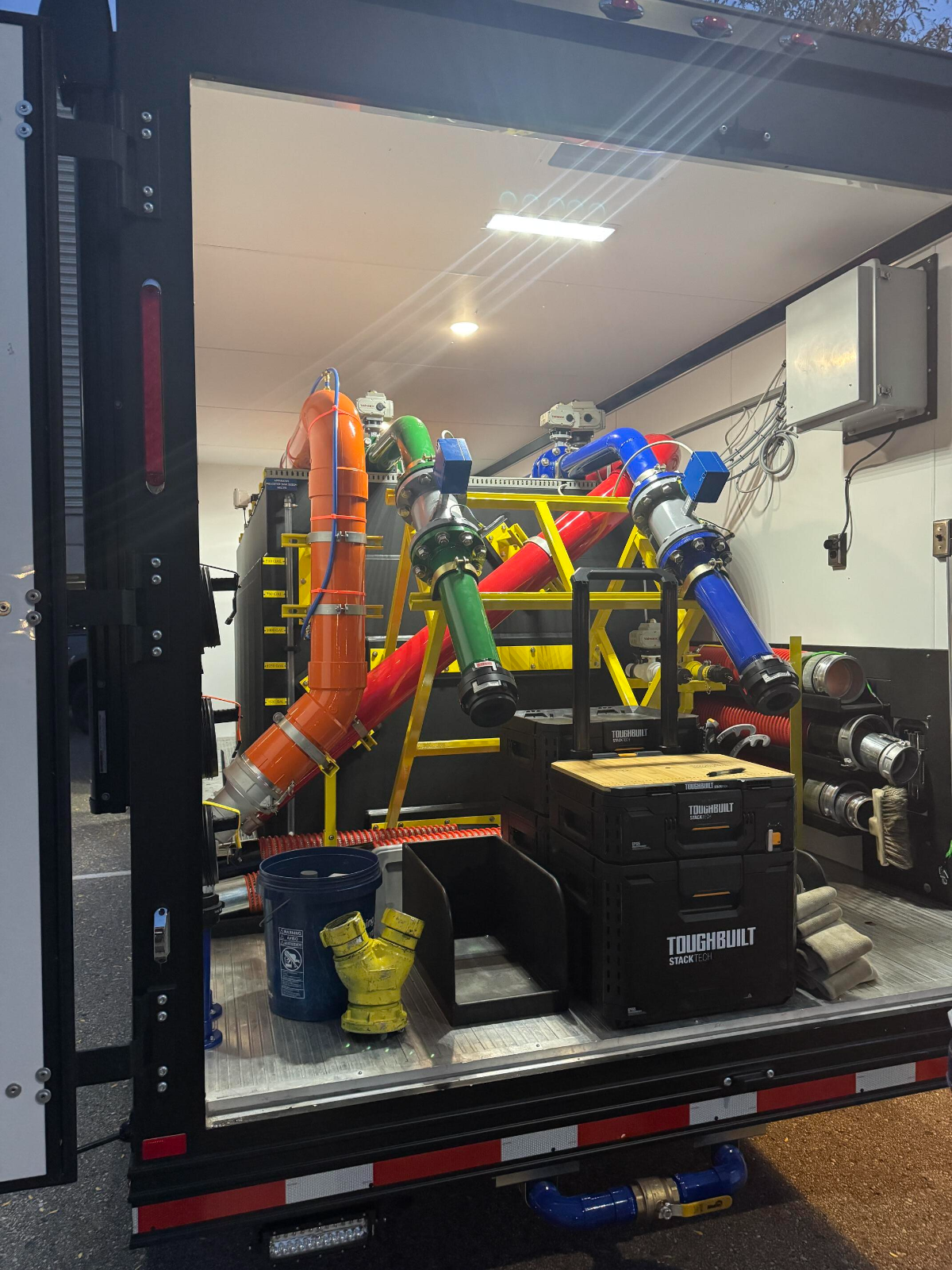 The interior of a trailer is filled with colorful decontamination equipment, hoses, ToughBuilt toolboxes, and various fittings organized for easy access.