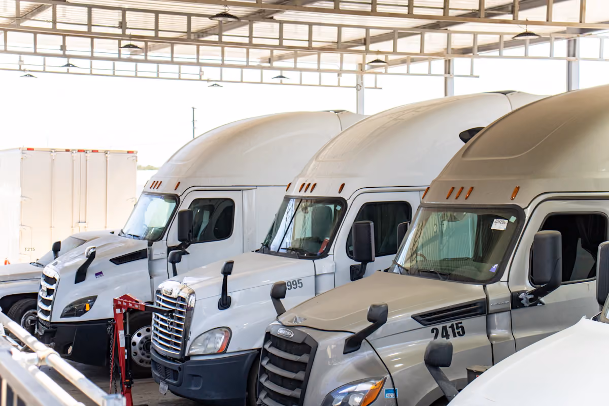 Three white semi-trucks parked side by side inside a covered truck maintenance facility.
