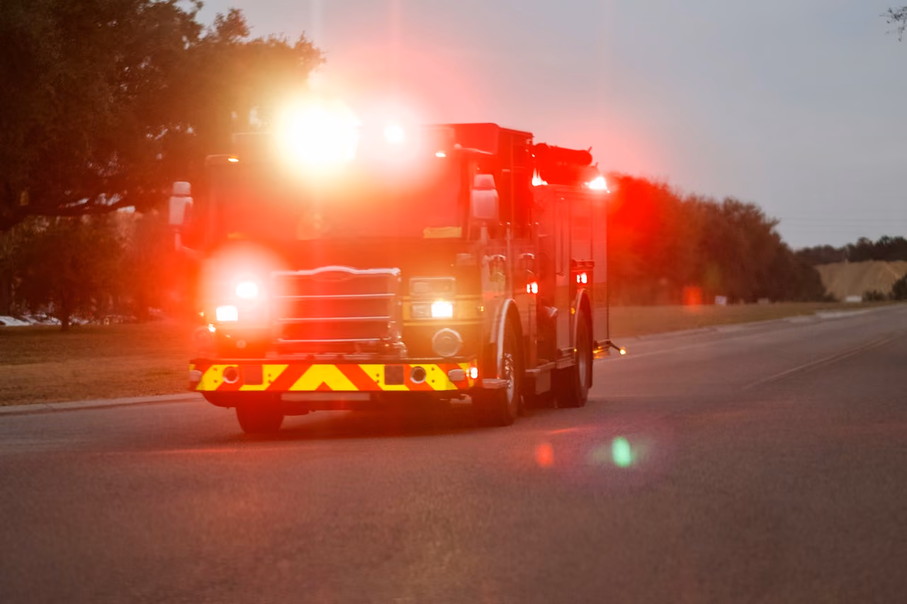 Fire truck with flashing emergency lights driving on a roadway at dusk, responding to an emergency call in low-light conditions.