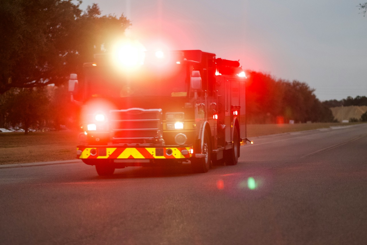 Fire truck with flashing emergency lights driving on a roadway at dusk, responding to an emergency call in low-light conditions.