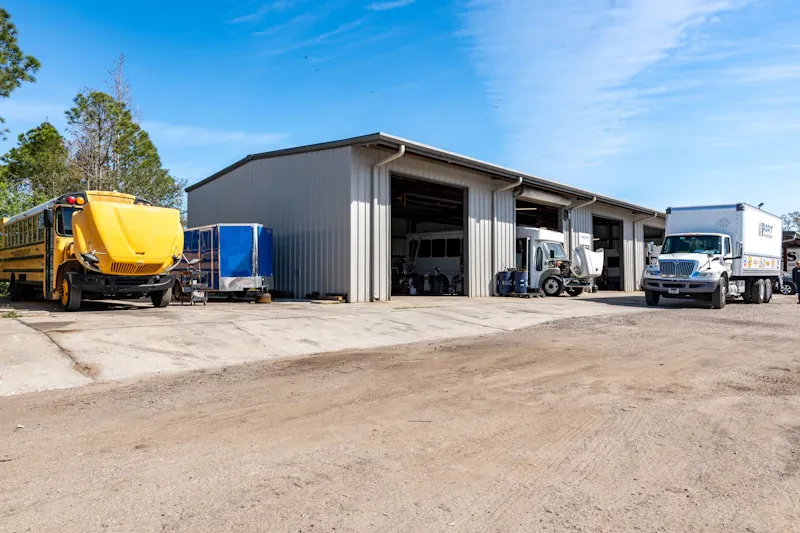 Heavy-duty truck repair facility with open service bays, a school bus, and commercial trucks parked outside for maintenance.