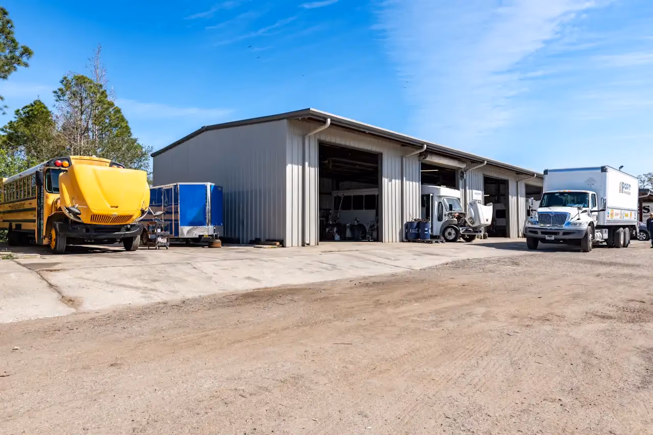 Heavy-duty truck repair facility with open service bays, a school bus, and commercial trucks parked outside for maintenance.