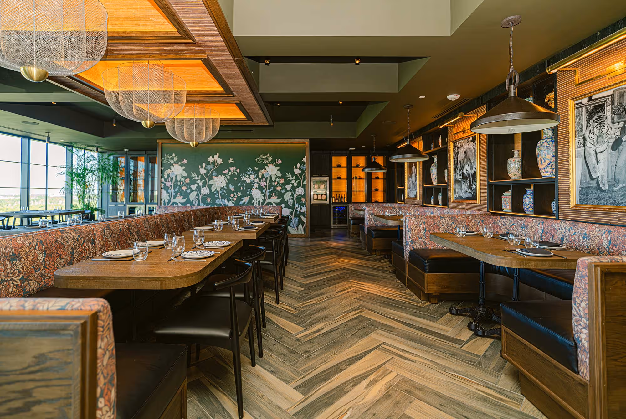 Natural light-filled restaurant with wood tables, leafy plants, and ceiling-mounted light fixtures.