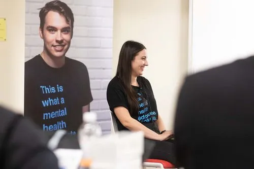 Speaker talking to off screen crowd with poster in the back wearing jack.org merch
