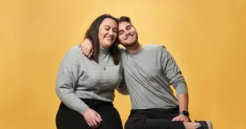 two bethere participants in grey shirts hugging in front of a yellow background