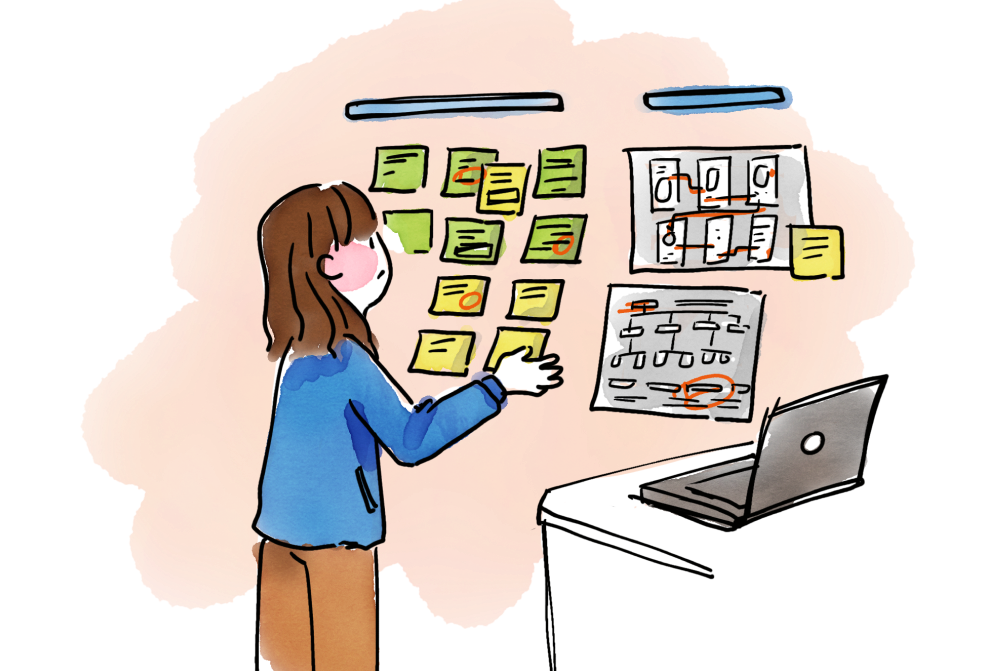 Person in blue jacket organizing sticky notes on an orange wall next to a laptop on a desk.