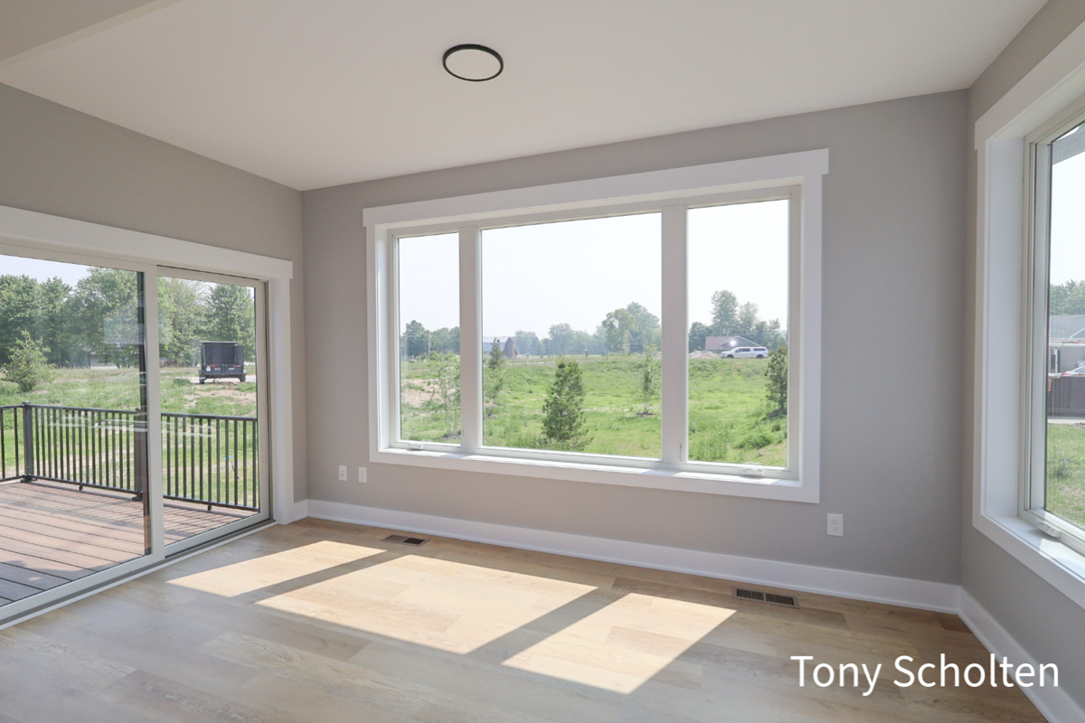 Unfurnished room with large windows and sliding glass door overlooking a green outdoor area and deck.