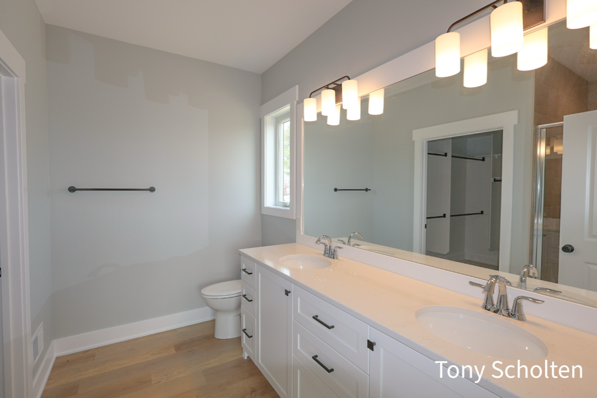 Modern bathroom with double sink vanity, large wall mirror, toilet, and a towel rack on a gray wall.