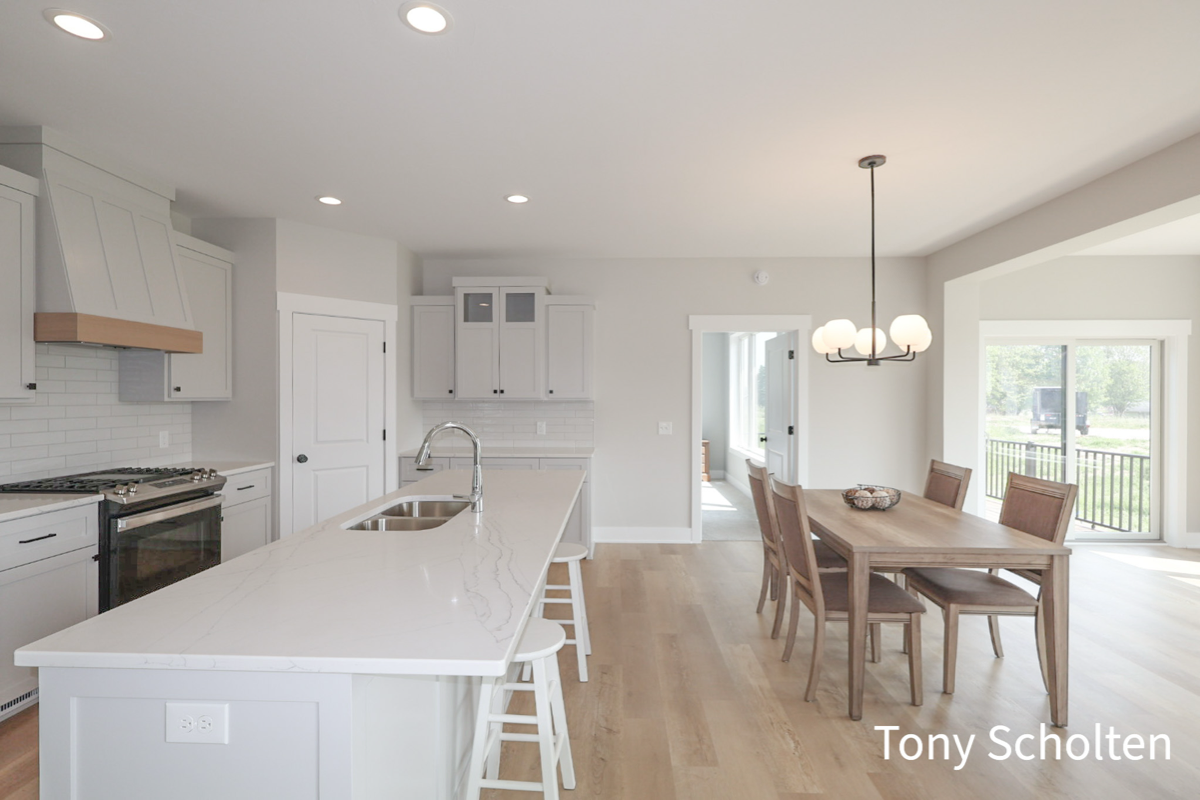 Modern kitchen with white cabinetry, a large marble island with sink and stools, adjacent to a wood dining table with six chairs under a hanging light fixture.
