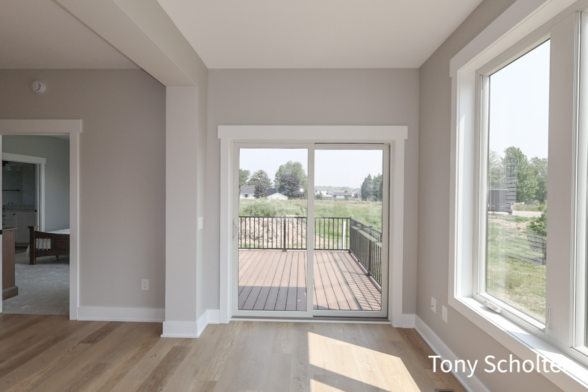 Unfurnished room with light wood flooring, beige walls, a sliding glass door opening to a wooden deck, and large windows letting in natural light.