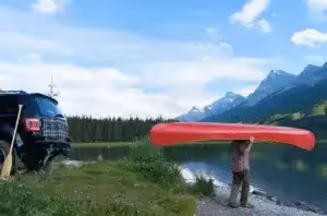 person carries kayak from car near lake