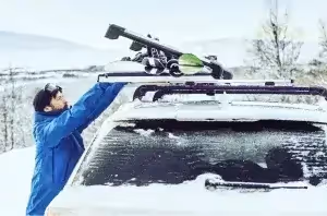 male attaching skis and snowboard to vehicle roof rack in winter