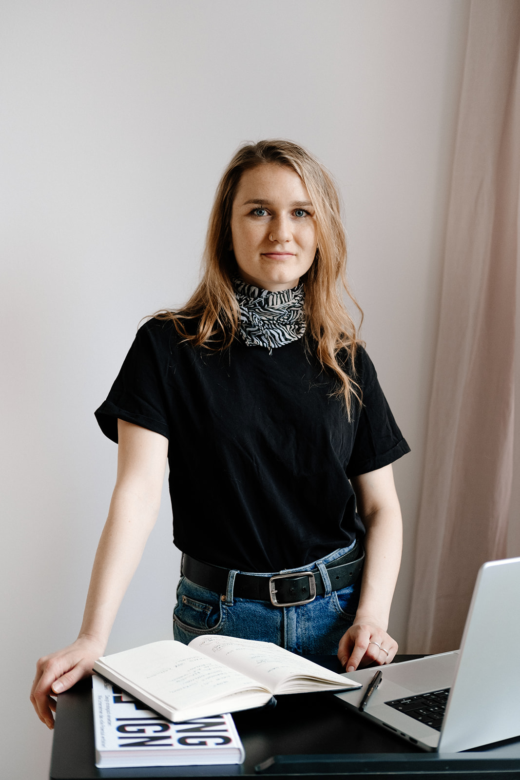 Eine Frau steht an einem Stehpult und blickt selbstbewusst in die Kamera. Auf dem Stehpult befinden sich ein Laptop, ein Notizbuch und ein Buch.