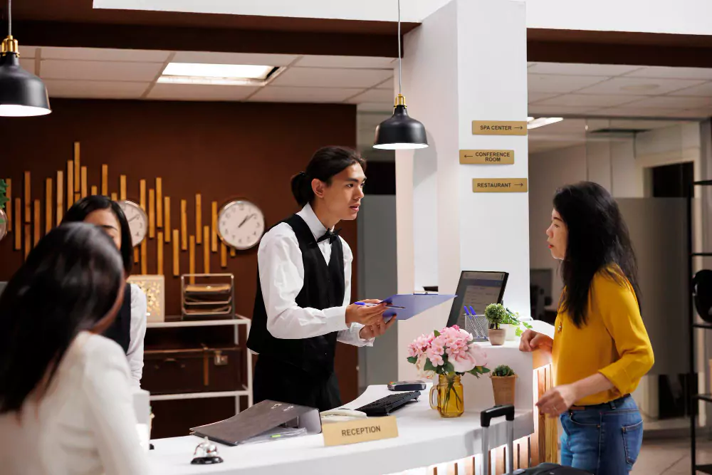 Tetamu hotel menerima borang pendaftaran daripada concierge lelaki Asia yang membantu.