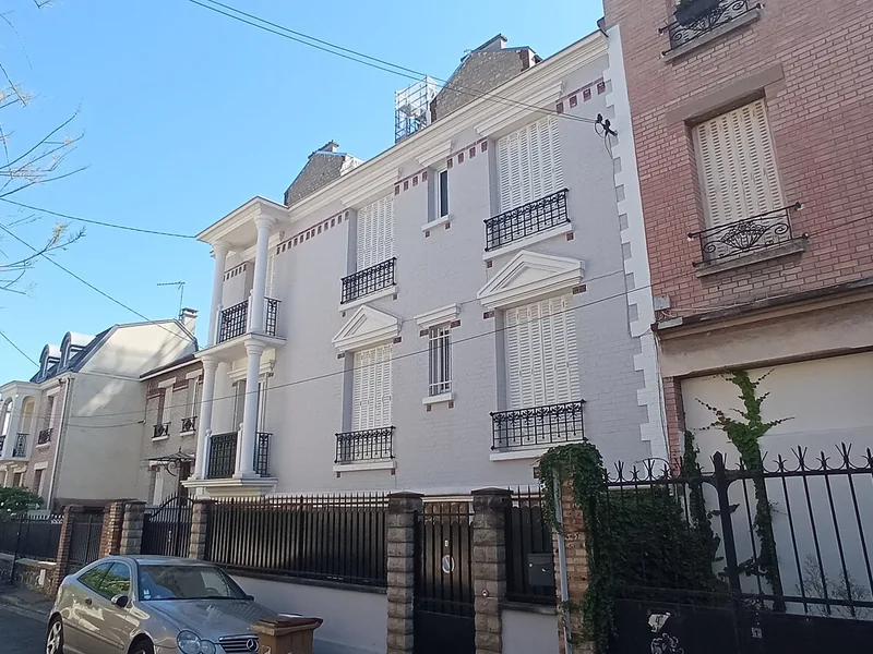 Petit immeuble blanc à balcons et grilles dans une rue de Colombes