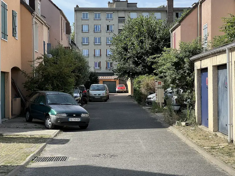 Allée bordée de maisons de ville et de garages, avec un immeuble au fond, à Saint-Denis