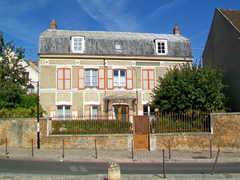 Maison ancienne aux volets orange derrière un muret de pierre, rue de Neuville à Cergy