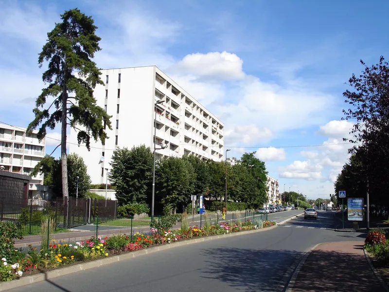 Immeuble blanc à balcons derrière des massifs de fleurs, rue de Paris à Franconville