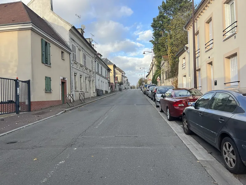 Rue de Sarcelles bordée de maisons de ville anciennes et de voitures garées