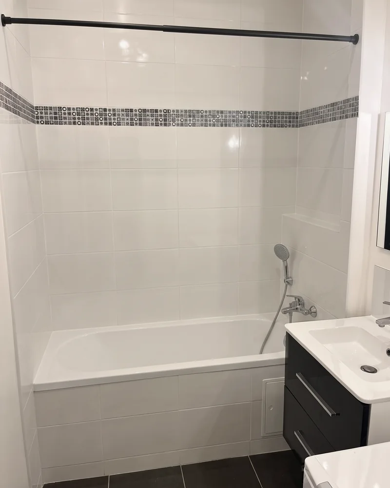 Avant&nbsp;: la&nbsp;baignoire sous une barre de&nbsp;rideau, à&nbsp;côté du&nbsp;meuble vasque noir