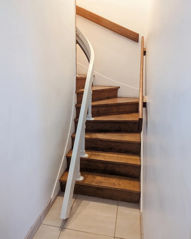 Après&nbsp;: le&nbsp;même escalier, avec le&nbsp;rail blanc du&nbsp;monte-escalier le&nbsp;long des marches