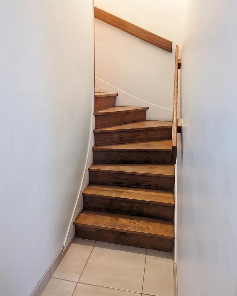 Avant&nbsp;: l'escalier en&nbsp;bois vu&nbsp;d'en&nbsp;bas, étroit et&nbsp;tournant, avec sa&nbsp;main courante
