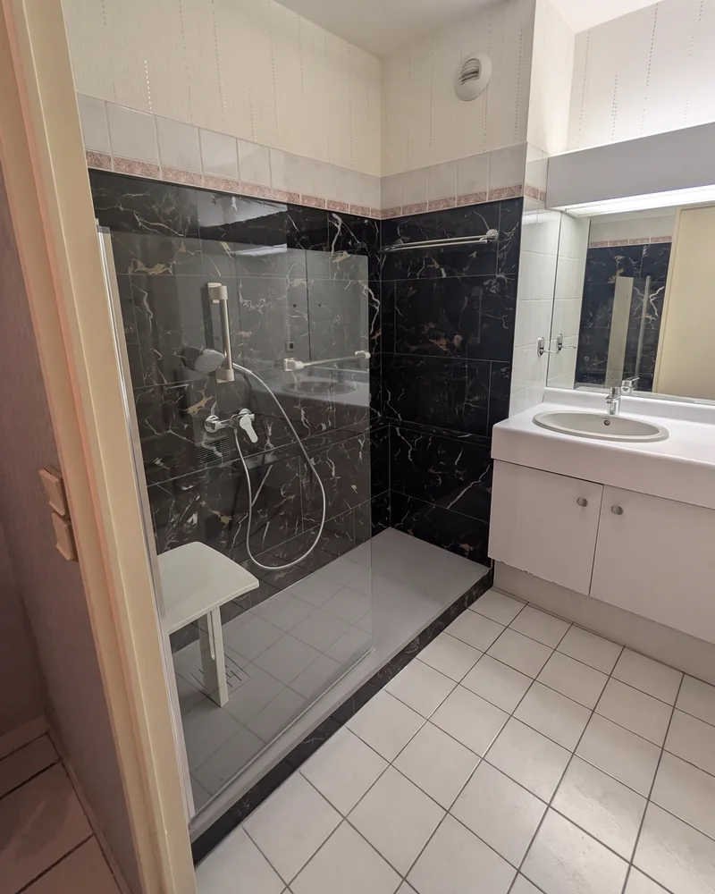 Après&nbsp;: la&nbsp;même salle de&nbsp;bain, avec une douche à&nbsp;paroi vitrée, un&nbsp;siège et&nbsp;une barre d'appui verticale