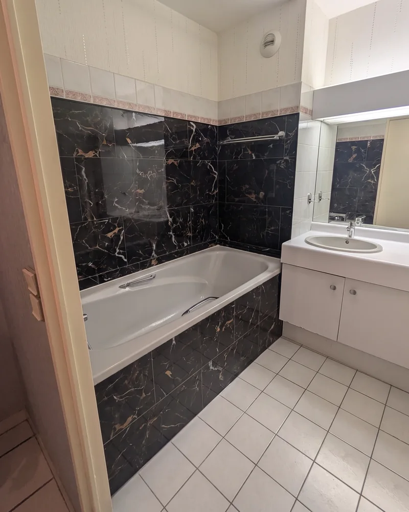 Avant&nbsp;: la&nbsp;salle de&nbsp;bain vue depuis la&nbsp;porte, avec la&nbsp;baignoire à&nbsp;gauche et&nbsp;le&nbsp;lavabo sur un&nbsp;meuble à&nbsp;droite