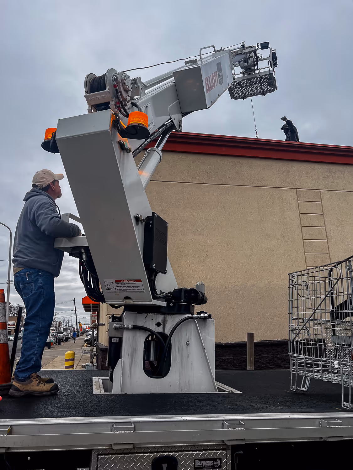 A worker operates a crane lift outside a building with another person on the roof.