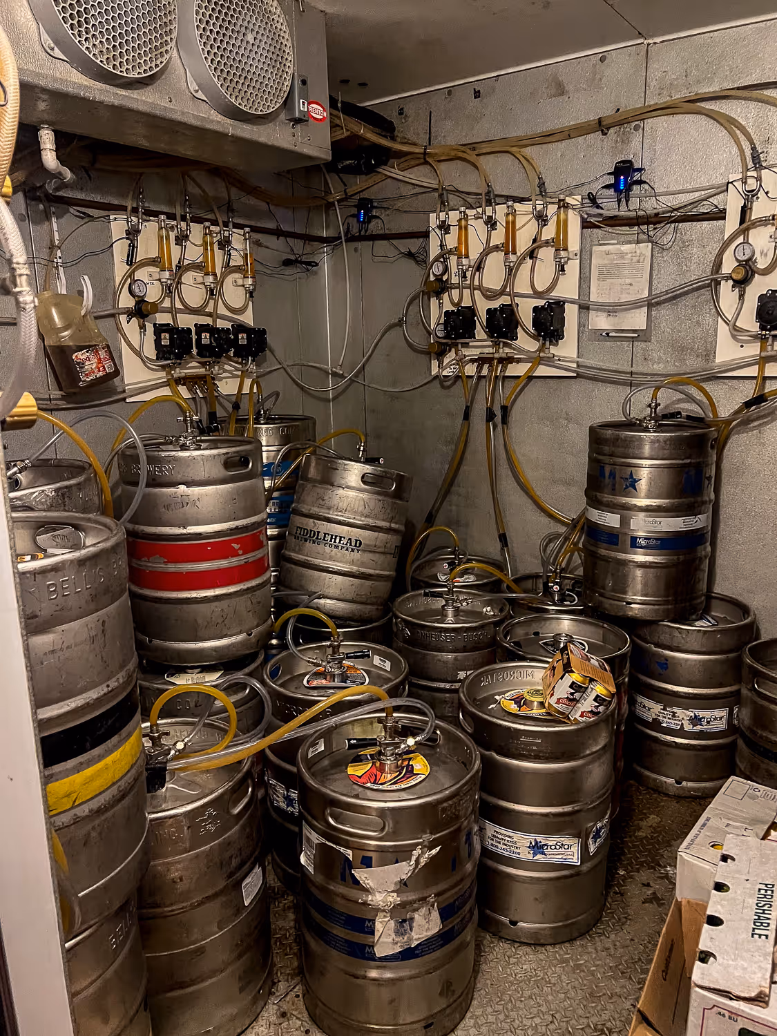 Multiple kegs with connecting hoses are stacked in a storage room, ready for use.