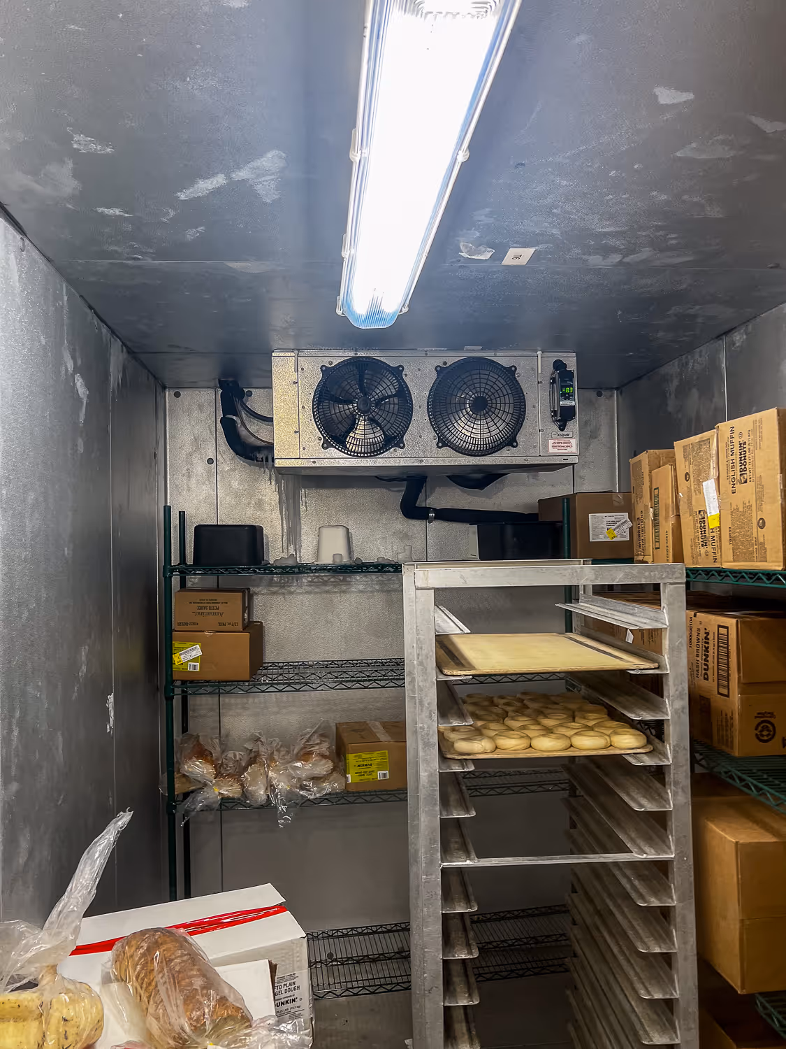 A walk-in cooler with racks of packaged food and a ceiling fan for cooling.