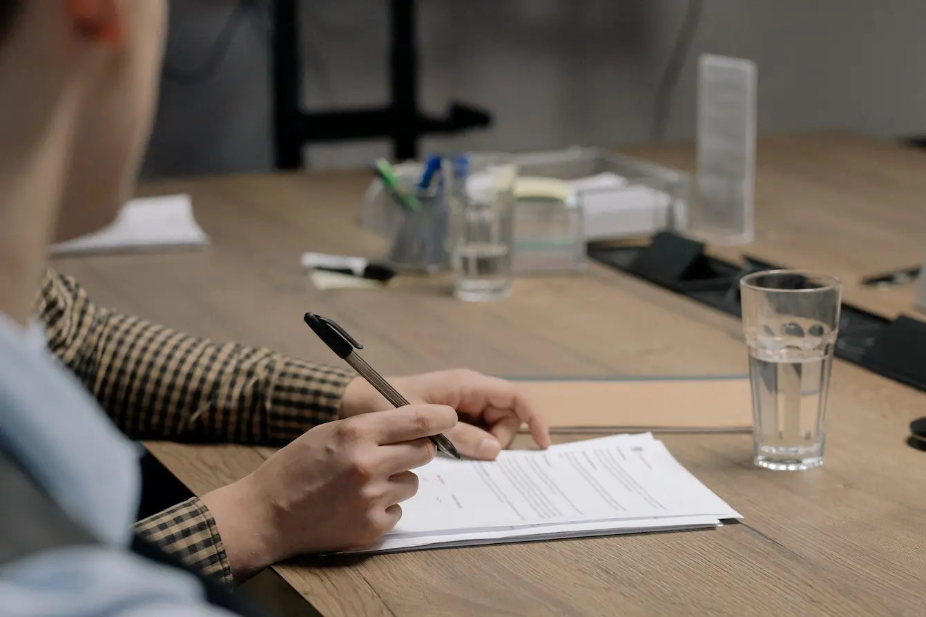 Personne en tenue professionnelle signant un document sur une table en bois dans un cadre de bureau