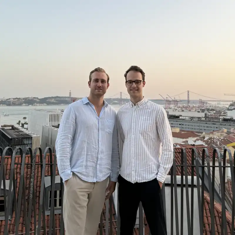 Simon Link and Sebastian Feit Founders of Bleisured, standing on the Miradouro de Santa Catarina in Chiado, in the background river Tejo and 25 of April bridge in Lisbon