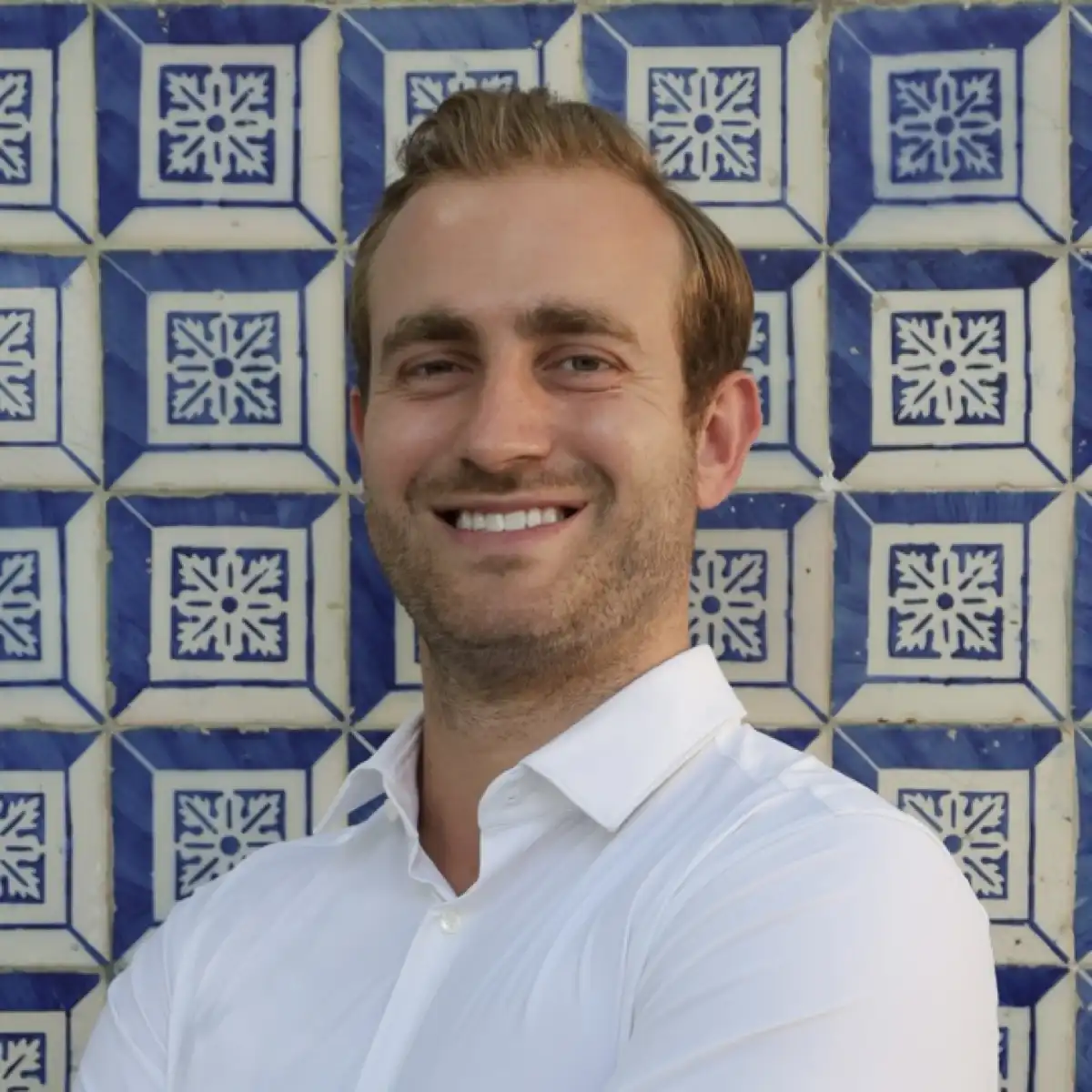 Profile picture of Sebastian Feit, one of the founders of Bleisured, in a white shirt, in front of blue Azulejo tiles in Lisbon